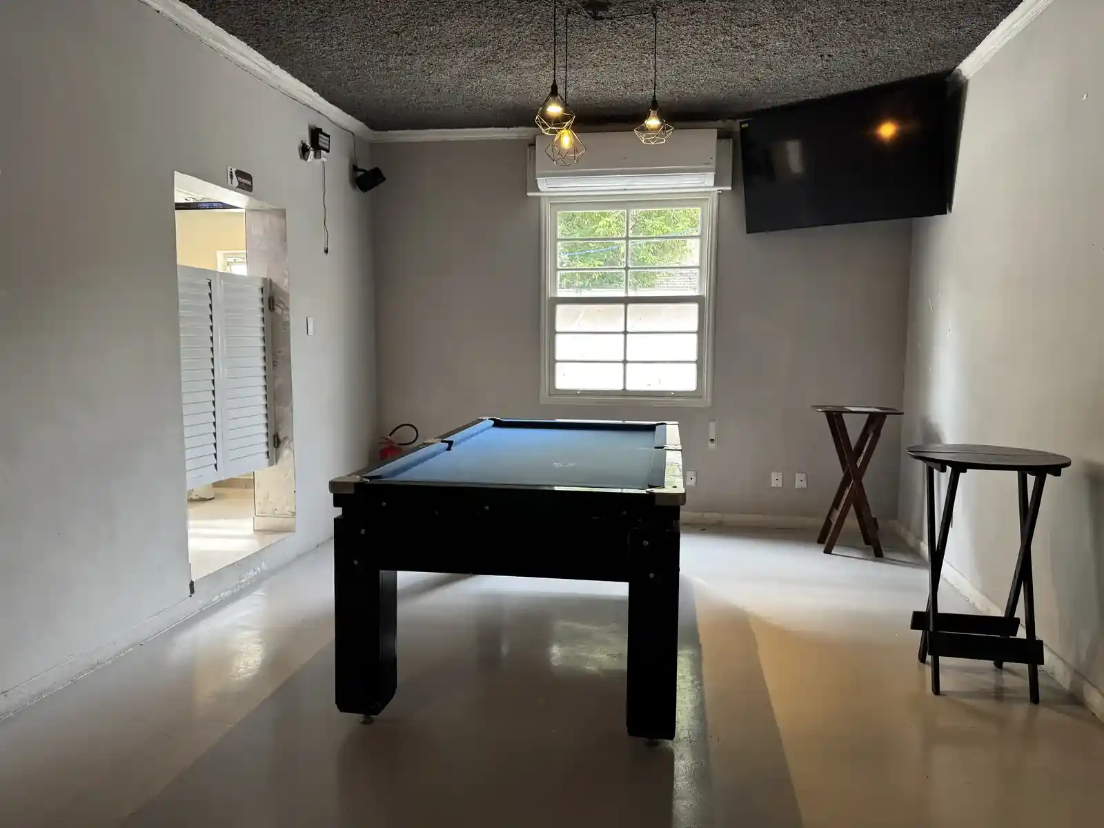 Sala de sinuca do Zora Bar em Santos, com mesa profissional, pendentes e TV na parede