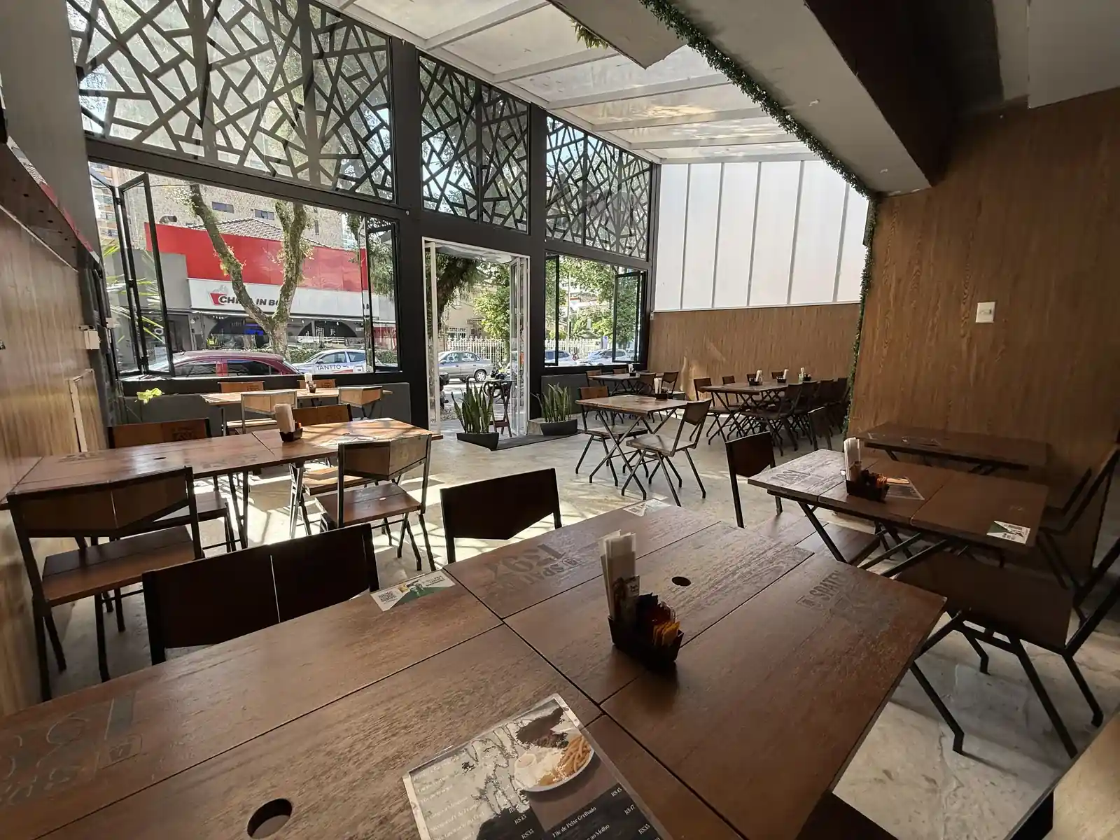 Salão do Zora Bar visto de dentro, com a fachada de vidro aberta para a rua gastronômica do Gonzaga