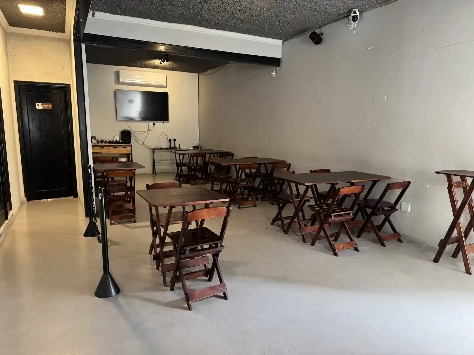Sala reservada de karaokê do Zora Bar em Santos, com telão, mesas de madeira e iluminação de trilho