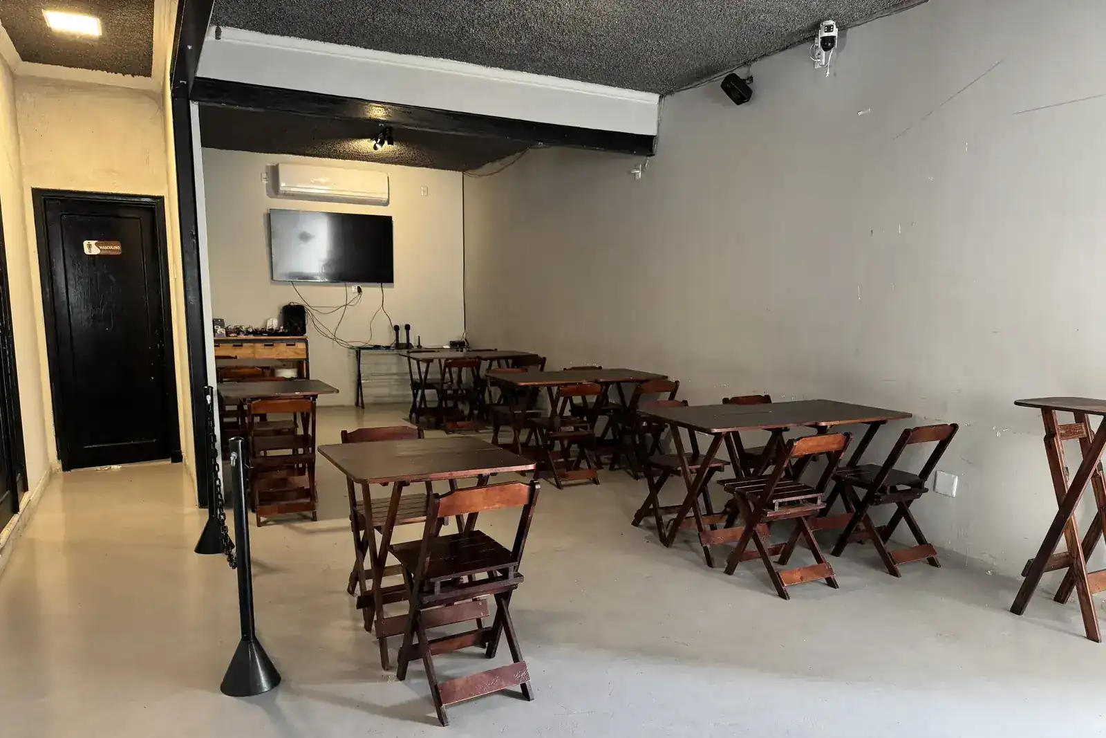 Ambiente de karaokê do Zora Bar com telão e mesas de madeira