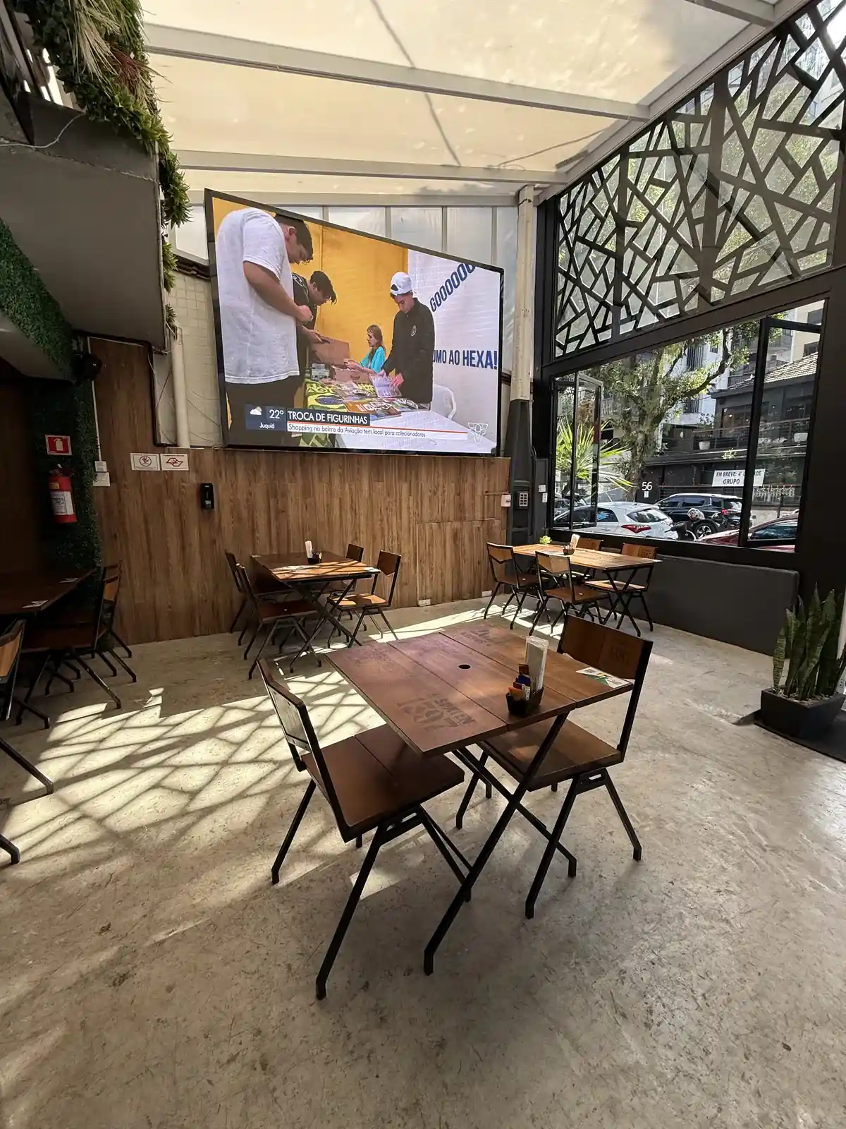 Telão do Zora Bar em Santos transmitindo jogo de futebol para o salão com mesas de madeira